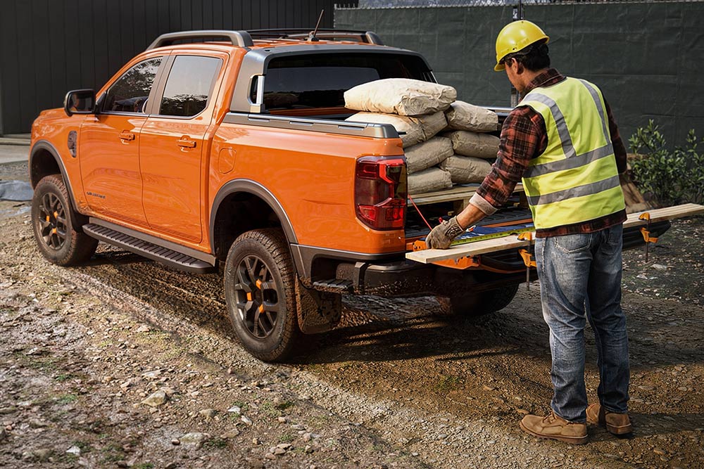 Ein Bauarbeiter lädt Ausrüstung auf die Ladefläche eines orangefarbenen Ford Ranger.