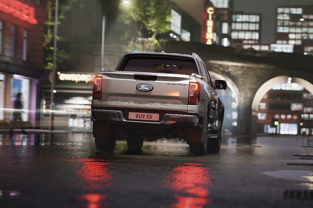 Heckansicht eines silbernen Ford Ranger, der nachts durch eine neonbeleuchtete Stadt fährt.