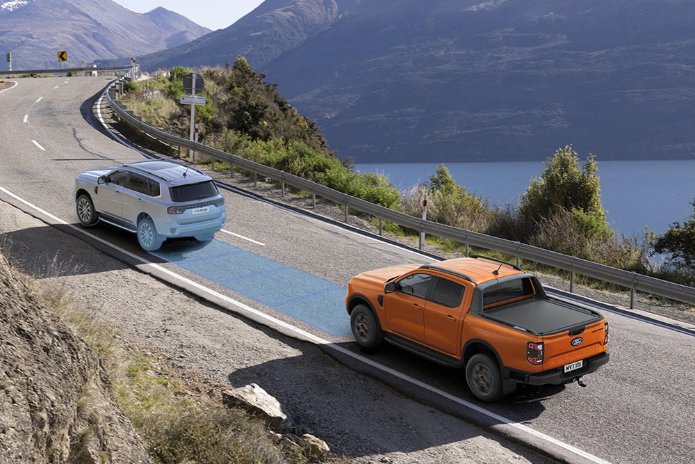 Ein orangefarbener Ford Ranger nutzt sein fortschrittliches Fahrerassistenzsystem auf einer Küstenstraße.