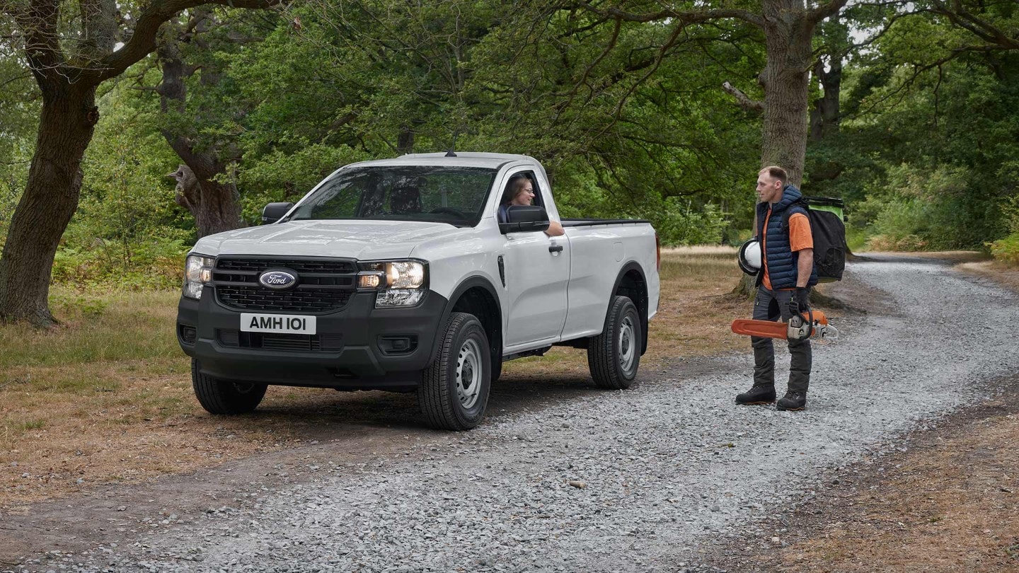 Ford Ranger in Weiß in der ¾-Frontansicht mit Fahrerin parkt auf Waldweg neben Waldarbeiter