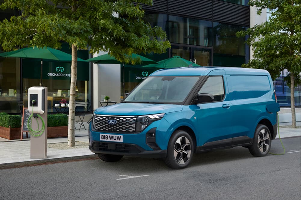 Blauer Ford E-Transit Courier in der 3/4-Frontansicht neben einer Ladestation.