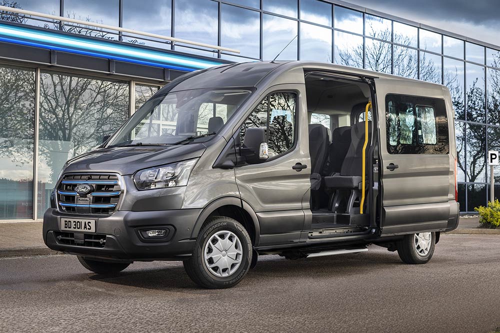 Seitenansicht eines grauen Ford Pro Transit mit geöffneten Türen, parkt vor einem modernen Gebäude.