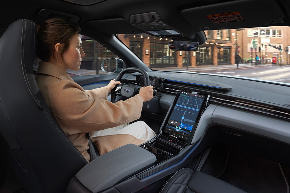 Eine Person fährt ein Ford-Fahrzeug, auf dem zentralen Touchscreen wird die Navigation angezeigt.