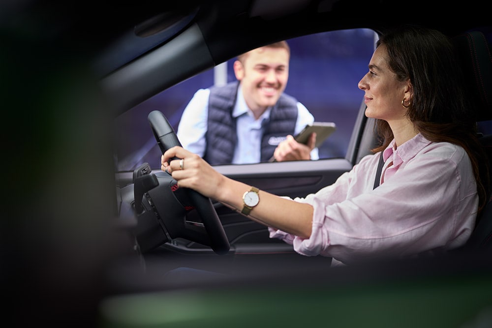 Eine Person auf dem Fahrersitz eines Ford-Fahrzeugs blickt auf einen Techniker mit Tablet.