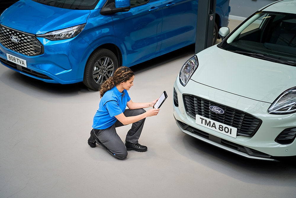 Ein Techniker kniet zwischen einem blauen Ford-Transporter und einem grauen Ford Puma und schaut auf ein Tablet.