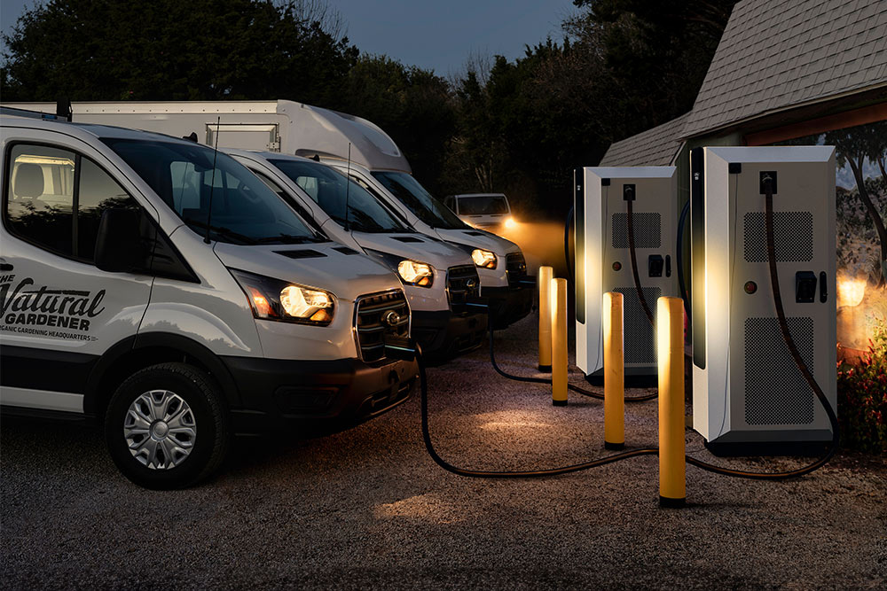 Evening scene of Ford electric vans charging at a power station.