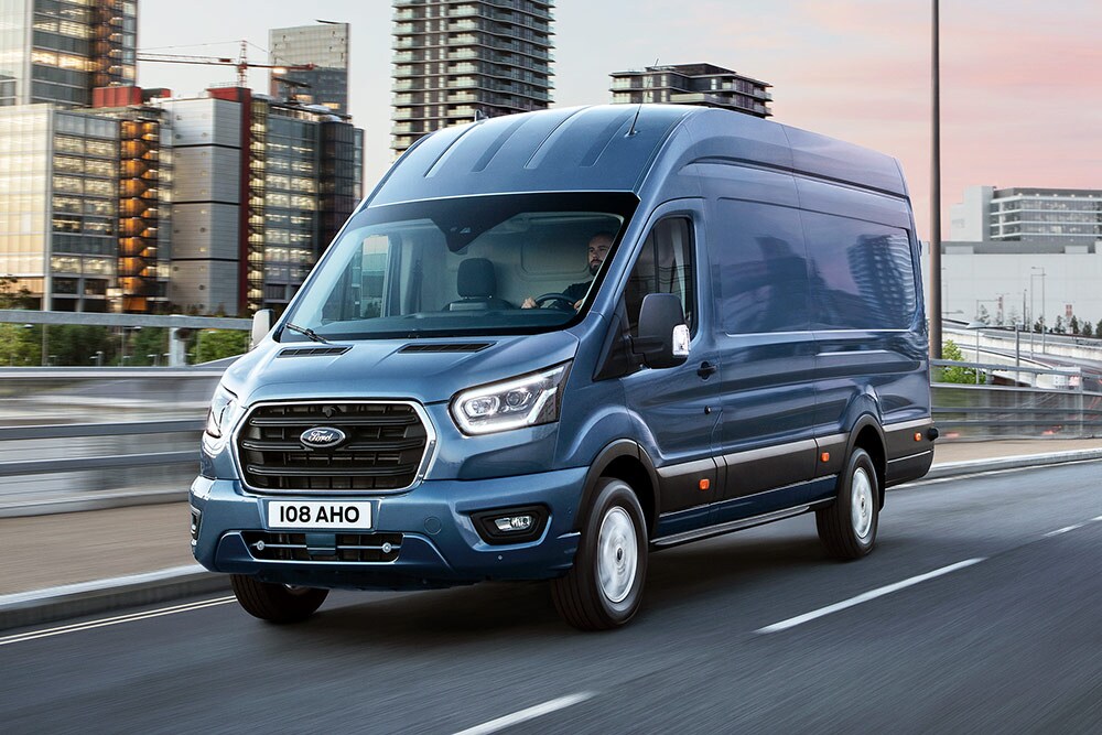 Ein Ford Transit fährt über eine Brücke, im Hintergrund eine bebaute Stadtlandschaft.