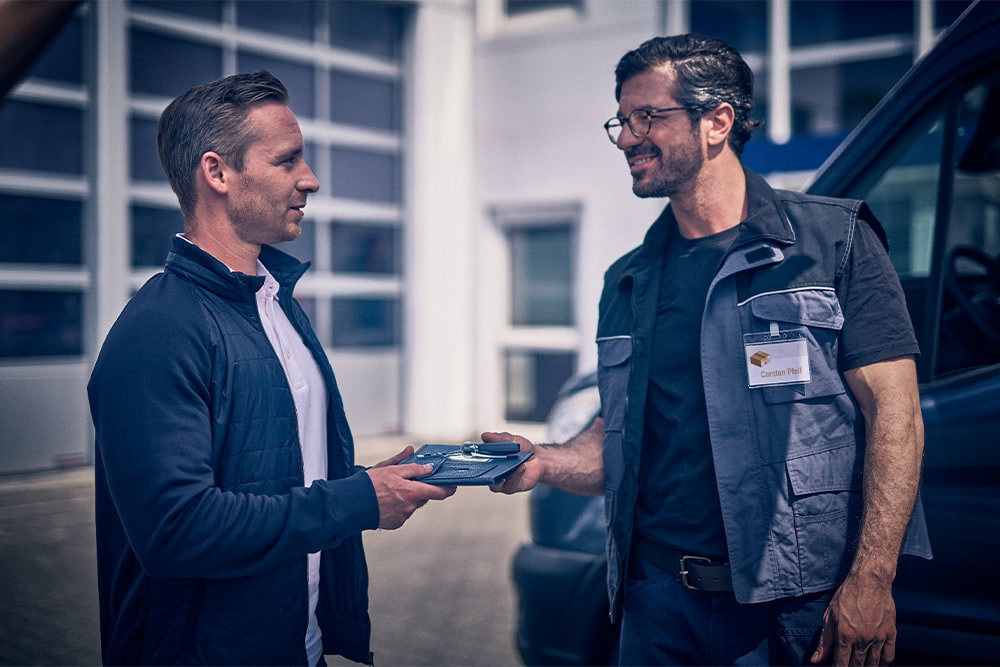 Zwei Männer schütteln sich vor einem Ford-Van die Hand und einer übergibt die Fahrzeugschlüssel.