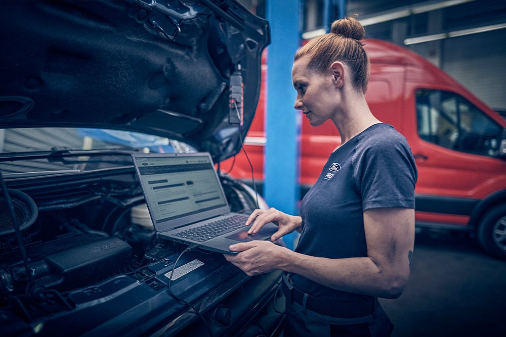 Eine Frau nutzt einen Laptop, der mit dem Motorraum eines Ford-Van in einer Garage verbunden ist.