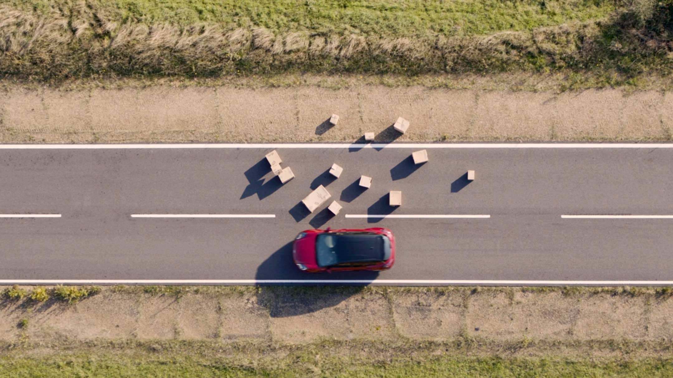 Ford Mustang Mach-E aus der Vogelperspektive weicht Boxen auf einer Landstraße aus