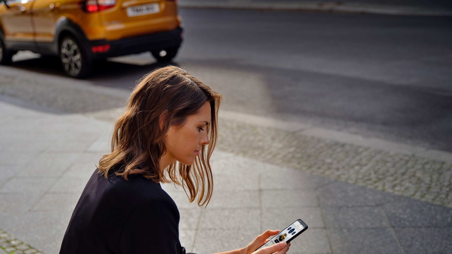 Frau sitzt am Straßenrand und schaut auf ihr Smartphone
