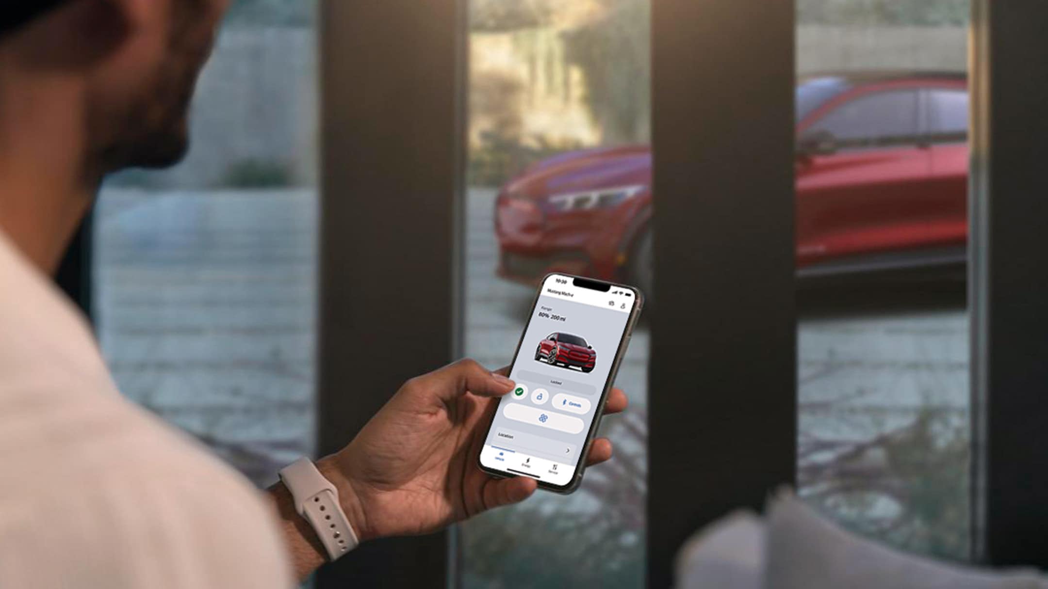 Ein Mann in seinem Wohnzimmer nutzt die Fahrzeug-Fernsteuerungsfunktionen in der FordPass-App für seinen in der Einfahrt geparkten Ford Mustang Mach-E