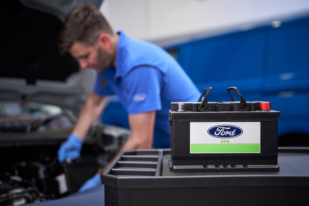 Ein Ford-Mechaniker, der an einem Automotor arbeitet, mit einer Ford-Autobatterie im Vordergrund.