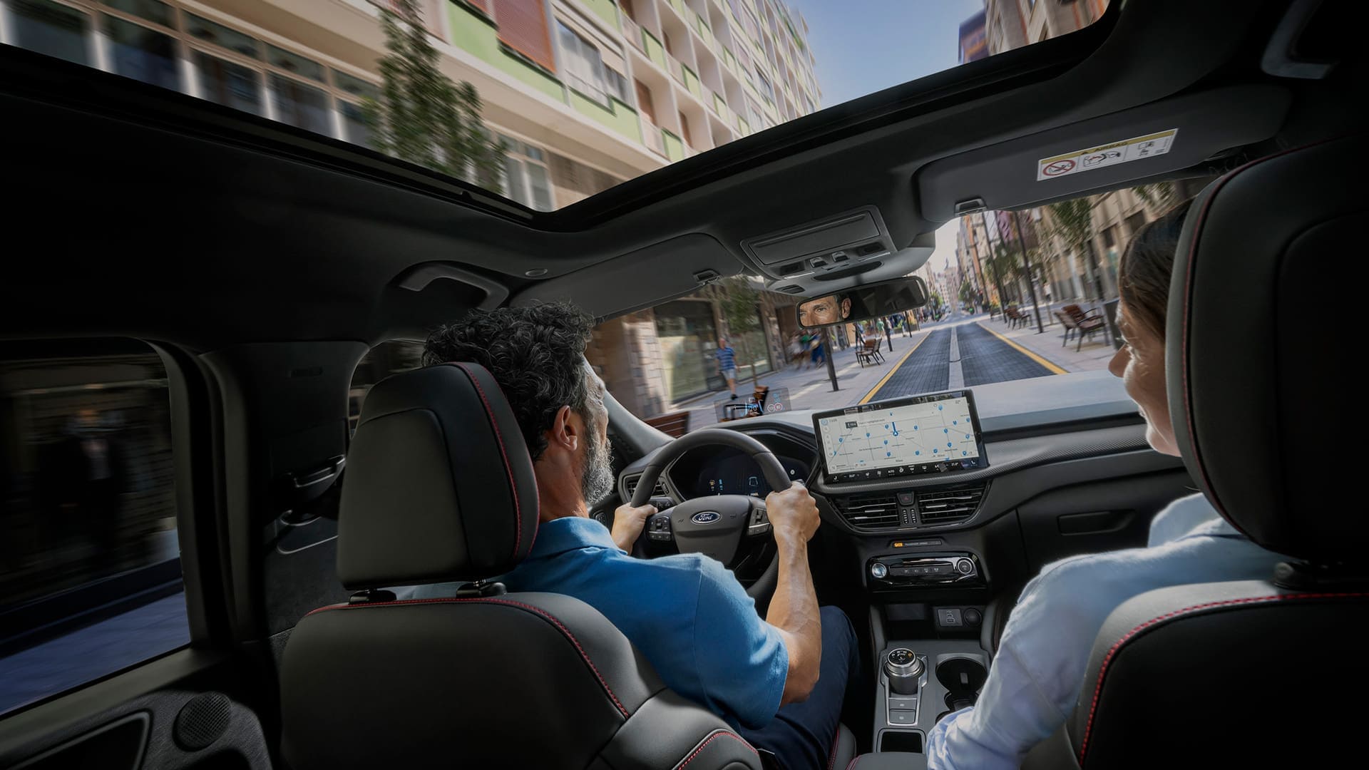 Fahrer und Beifahrerin in einem Ford nutzen SYNC auf dem digitalen Display zur Stadt Navigation.