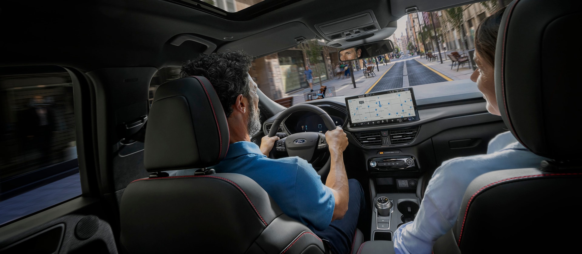 Fahrer und Beifahrerin in einem Ford nutzen SYNC auf dem digitalen Display zur Stadt Navigation.