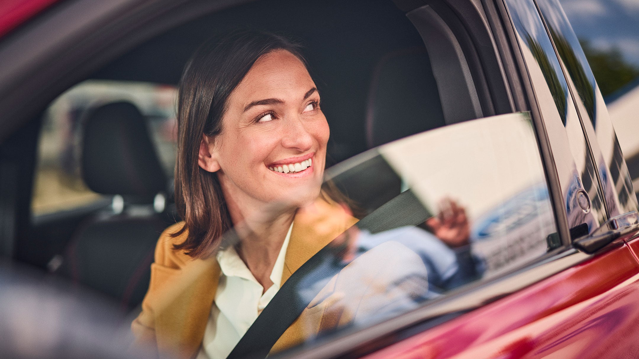 Eine lächelnde Frau, die in einem roten Ford sitzt.