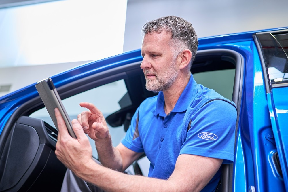 Ein Ford-Techniker sitzt in einem blauen Ford-Fahrzeug und nutzt ein Tablet, um Fahrzeugsysteme zu überprüfen.