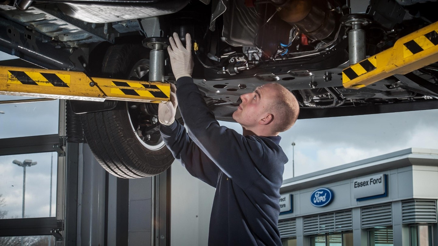 KFZ-Mechaniker prüft Fahrzeug auf Hebebühne