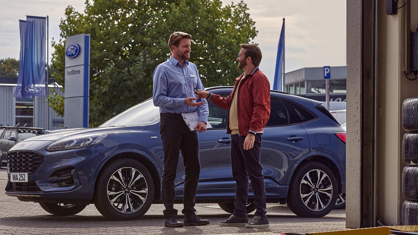 Lächelnder Mann mit lächelndem Ford-Servicemitarbeiter bei Fahrzeugabgabe