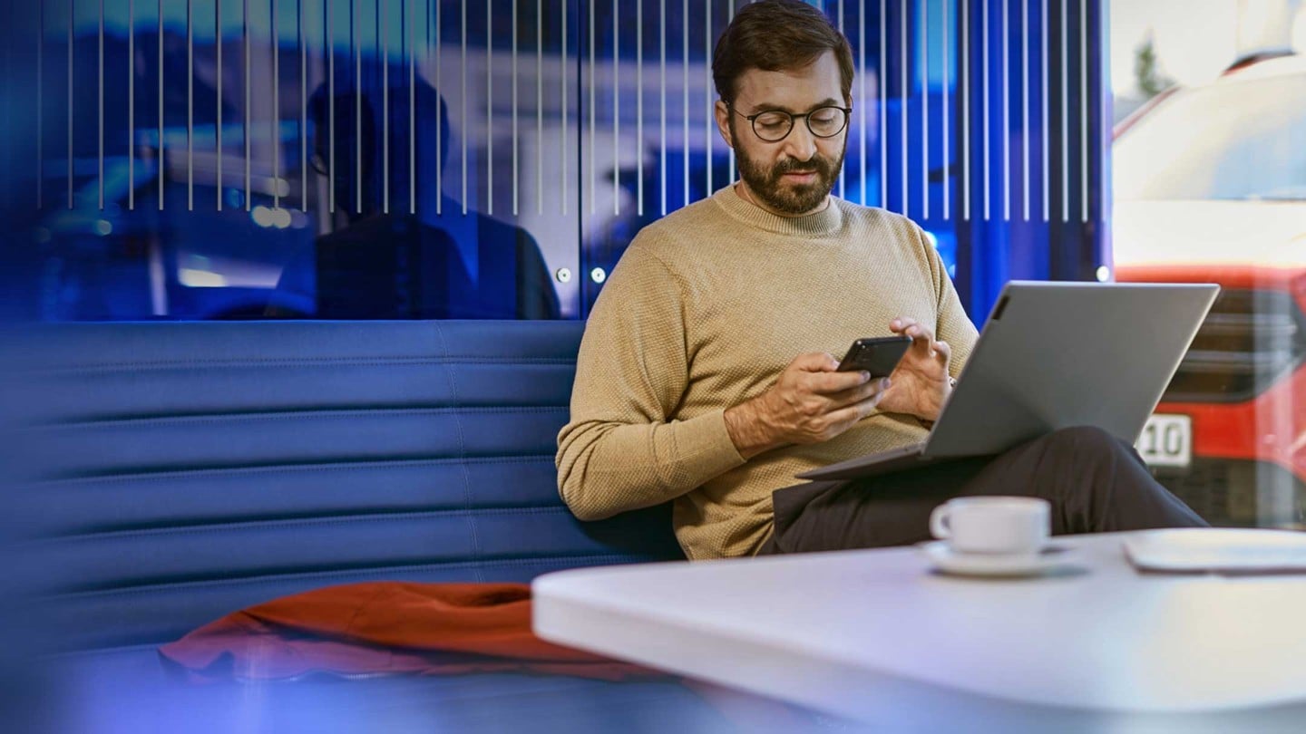 Eine Person sitzt an einem Schreibtisch mit einem Laptop und einem Smartphone in einer modernen Büroumgebung