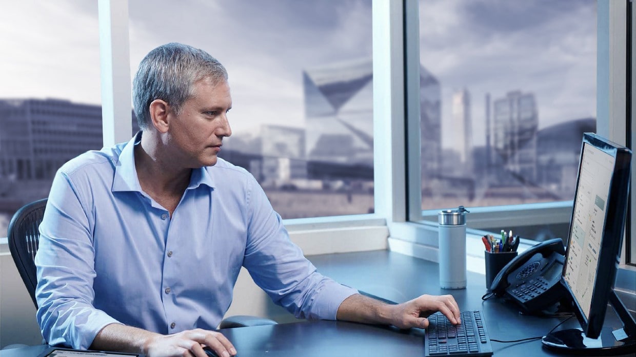 Mann sitzt in einem Büro am Schreibtisch und arbeitet am PC