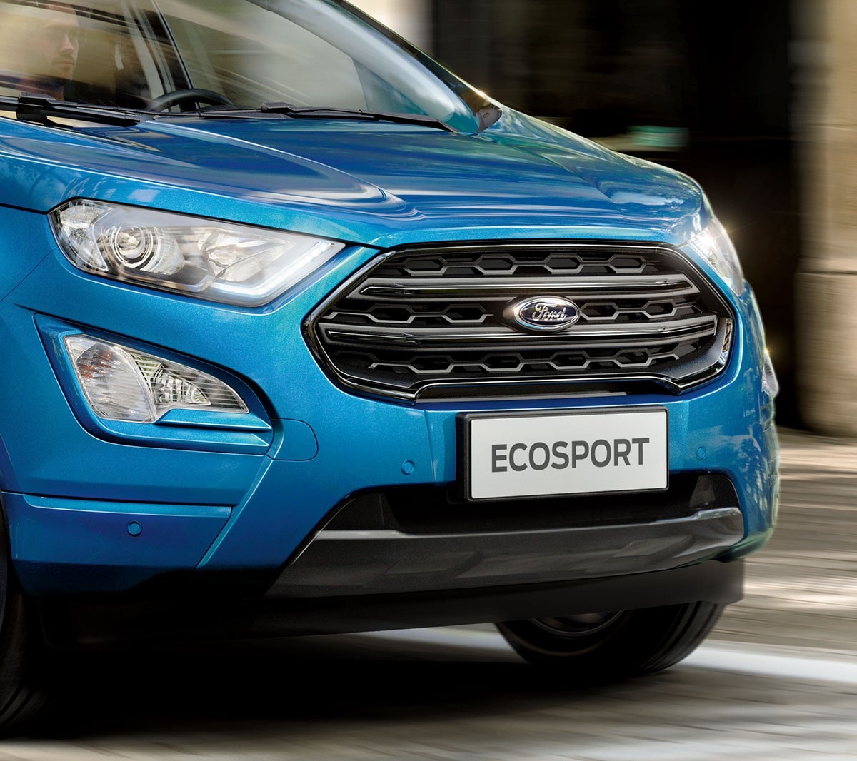 Ford EcoSport in Blau. Seitenansicht. Parkend auf einem Platz mit Menschen und Gebäuden im Hintergrund